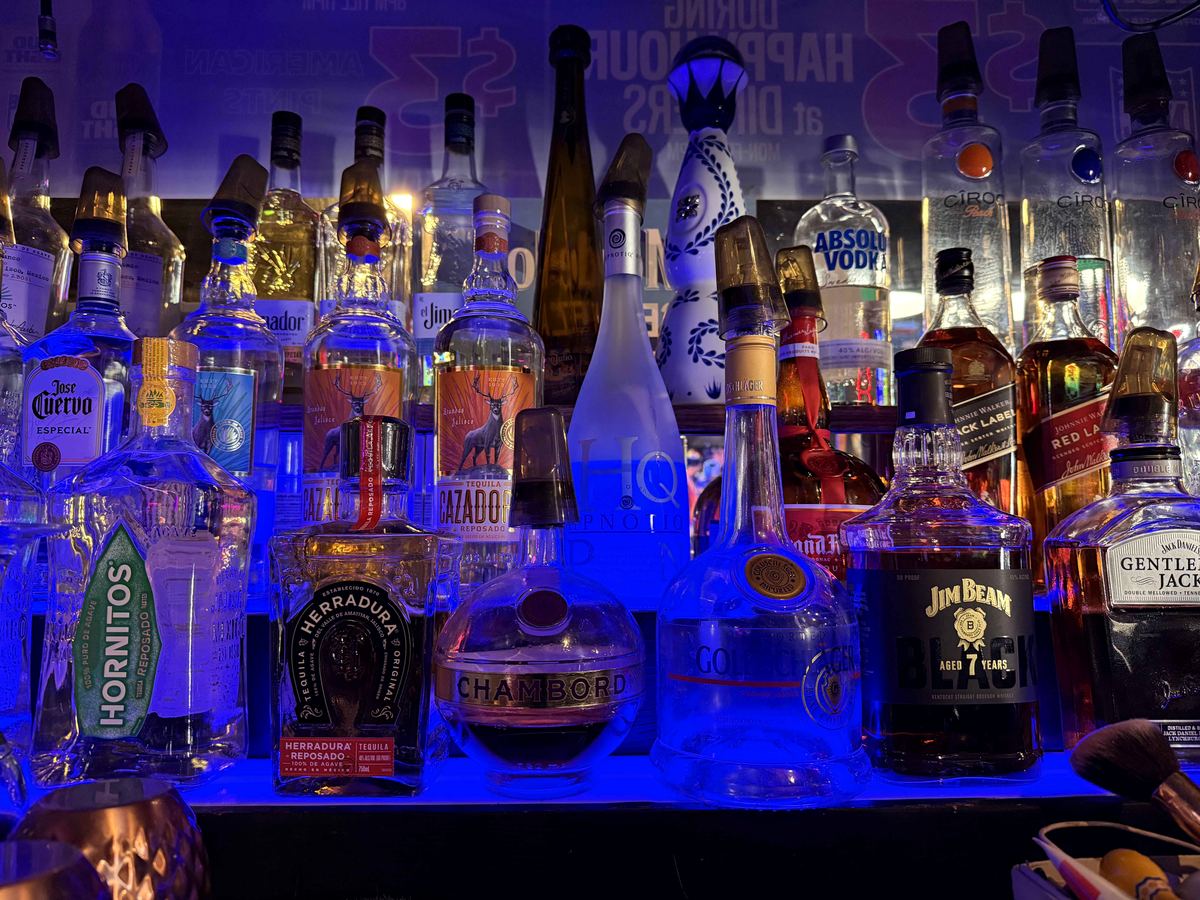 Back bar at Dingers Sports Bar illuminated by electric cobalt LED strip. Spirits including Hornitos, Herradura, Patron, Gentleman Jack, Jim Beam, Absolut Vodka, and Chambord on the shelves.