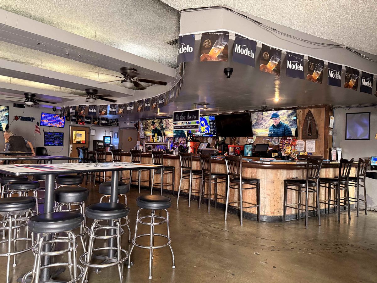 Full bar at Dingers Sports Bar. Modelo banner bunting strung across the ceiling, bar counter with tap handles, multiple TVs showing live sports.