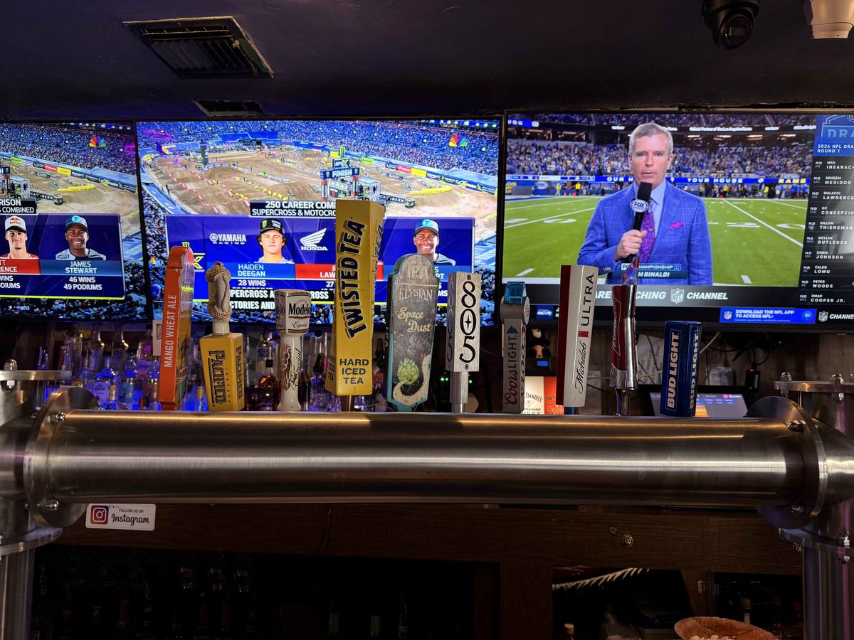 Tap handles at Dingers Sports Bar with two large TVs visible directly behind showing different live sports broadcasts simultaneously.