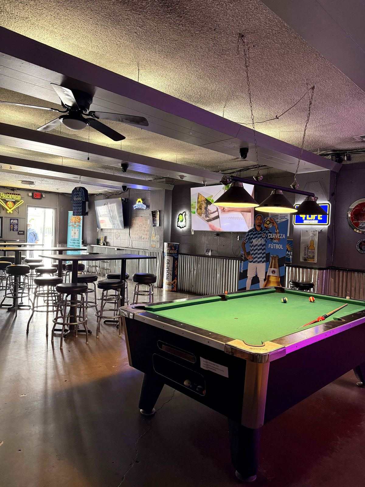 Pool room at Dingers at night. Back wall shows IPA red neon sign, TUF yellow neon, projector mount visible on ceiling.