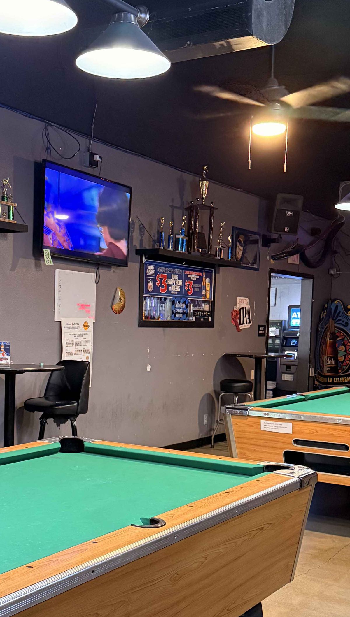 Two pool tables at Dingers under hanging lamps, with the trophy shelf on the wall behind them.